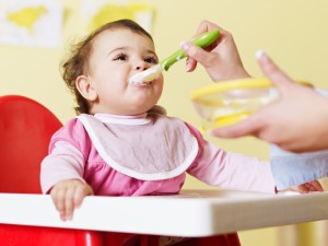 mom giving homogenized food to her daughter on high chair. Horizontal shape